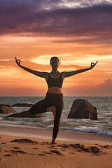Woman yoga position arms raised on tropical sea coast or ocean beach outdoors at sunset