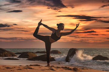 Silhouette slim woman does yoga on tropical sea coast or ocean beach outdoors on sunset