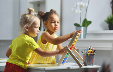 children of different races sit together at the table and count on the abacus