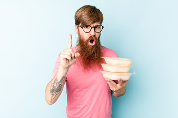 Young caucasian man holding a tupper ware isolated on blue background having an idea, inspiration concept.