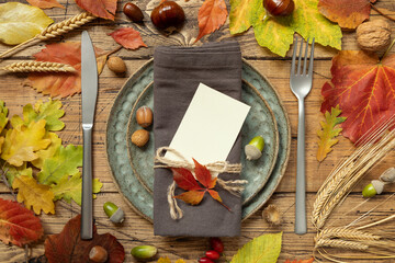 Autumn rustic table setting with blank place card between colorful leaves and berries top view,...