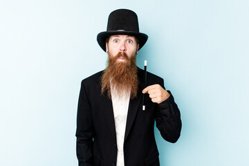Fototapeta premium Young magician man isolated on blue background shrugs shoulders and open eyes confused.