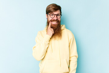 Young caucasian red-haired man isolated on blue background smiling happy and confident, touching chin with hand.