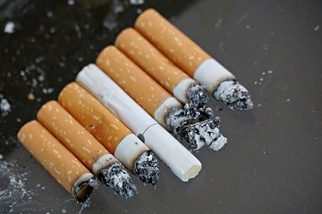cigarette buts on dark glass background, smoking issue concept