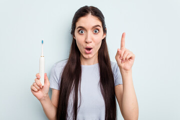 Young caucasian woman holding a electric toothbrush isolated on blue background having an idea, inspiration concept. © Asier