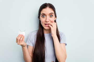 Fototapeta premium Young caucasian woman holding teeth whitener isolated on blue background biting fingernails, nervous and very anxious.