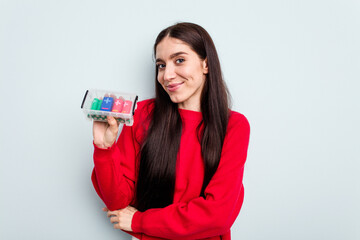 Young caucasian woman holding a batteries box isolated on blue background laughing and having fun.