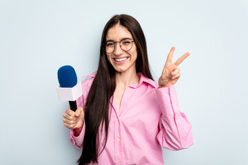 Fototapeta na wymiar Young caucasian tv presenter woman isolated on blue background joyful and carefree showing a peace symbol with fingers.