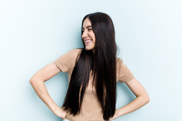 Obraz premium Young caucasian woman isolated on blue background laughs happily and has fun keeping hands on stomach.