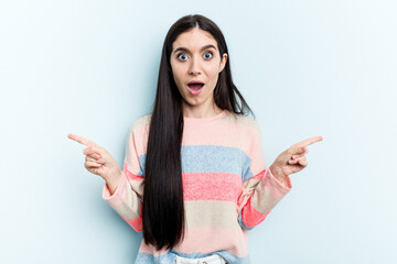 Naklejka premium Young caucasian woman isolated on blue background pointing to different copy spaces, choosing one of them, showing with finger.