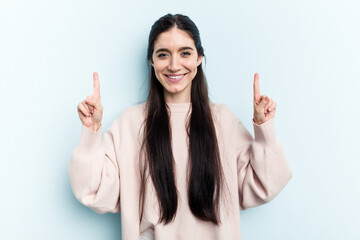 Young caucasian woman isolated on blue background indicates with both fore fingers up showing a...