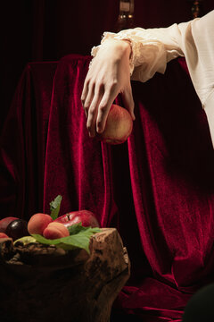 Closeup male hand with red apple over dark vintage background. Italian baroque style, art, creativity, vintage