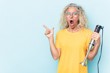 Middle age woman holding a blender isolated on blue background pointing to the side