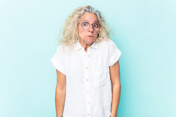 Middle age caucasian woman isolated on blue background shrugs shoulders and open eyes confused.