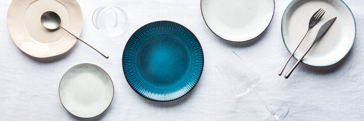 Modern tableware panorama with a vibrant blue plate, cutlery, and glasses, overhead flat lay shot. Trendy dinnerware on tablecloth - obrazy, fototapety, plakaty