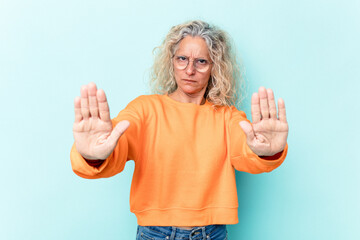 Middle age caucasian woman isolated on blue background standing with outstretched hand showing stop sign, preventing you.