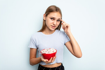 Young caucasian girl eating cereals isolated on blue background showing a disappointment gesture with forefinger.