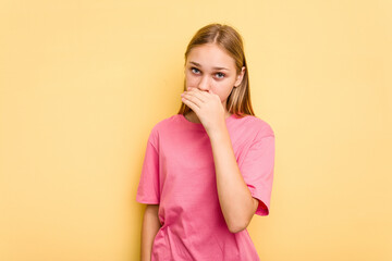 Young caucasian girl isolated on yellow background covering mouth with hands looking worried.