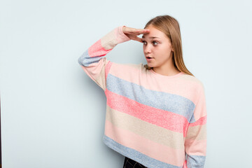 Young caucasian girl isolated on blue background looking far away keeping hand on forehead.