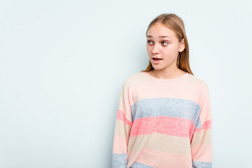 Young caucasian girl isolated on blue background being shocked because of something she has seen.