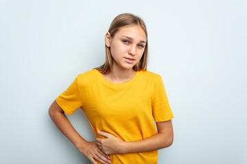 Young caucasian girl isolated on blue background having a liver pain, stomach ache.