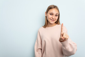 Young caucasian girl isolated on blue background showing number one with finger.