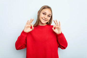 Young caucasian girl isolated on blue background cheerful and confident showing ok gesture.