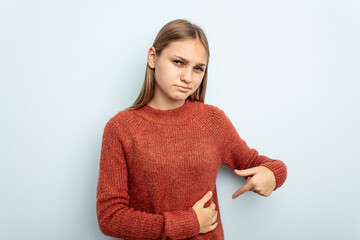 Young caucasian girl isolated on blue background having a liver pain, stomach ache.