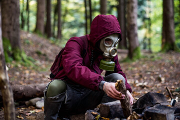 a male in a gas mask and a cherry jacket sits in the middle of the forest and starts a fire....