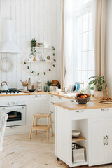 Modern large white Scandinavian kitchen with large window. Light stylish kitchen interior with kitchen accessories. Cooking hood, built-in oven, sink with water tap, potted plants. Empty space.