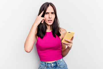 Young caucasian woman holding mobile phone isolated on white background showing a disappointment gesture with forefinger.