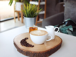 A cup hot latte coffee art with its bean and cup of hot tea on a wooden board on white table. With...