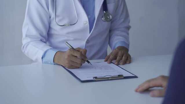 Close-up view Male doctor, unknown name, therapist, male doctor in white dress, sitting at the table, consulting the patient, complaining, giving medical advice, explaining, treatment table, prescript