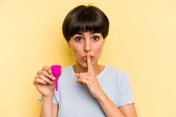 Young caucasian woman holding a menstrual cup isolated on yellow background keeping a secret or asking for silence.