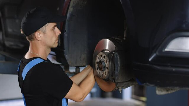 Car mechanic in blue overalls replacing car wheel brake shoes of lifted automobile ac repair service station. Mechanic repairing car at his workshop. Auto mechanic checking vehicle