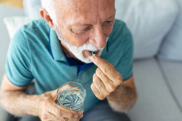 Senior man takes pill with glass of water in hand. Stressed mature man drinking sedated...