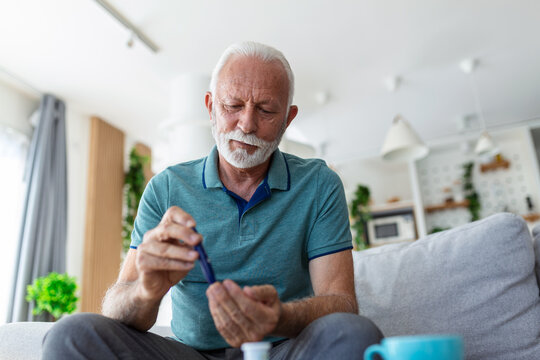 Mature man testing for high blood sugar. Man holding device for measuring blood sugar, doing blood sugar test. Senioir man checking blood sugar level by glucometer and test stripe at home