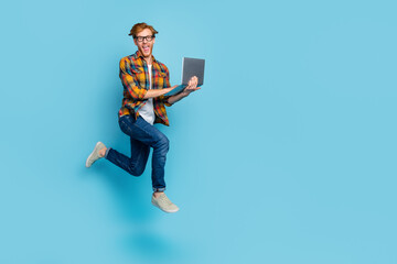 Fototapeta na wymiar Photo of funky positive guy with ginger hairstyle dressed plaid shirt holding laptop flying running isolated on blue color background