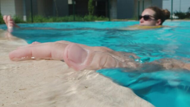 I run my hand over the stone tiles in the pool, a girl in the background. Close-up. Slow motion