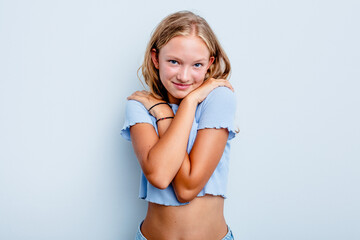 Naklejka premium Caucasian teen girl isolated on blue background hugs, smiling carefree and happy.