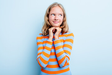 Caucasian teen girl isolated on blue background keeps hands under chin, is looking happily aside.