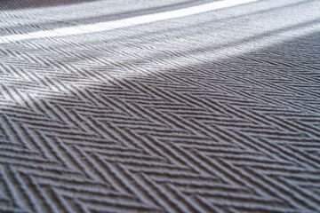 Inclined beams of light fall on a textured bedspread with a zig-zag pattern. A close-up view of the fabric. A shallow depth of field.