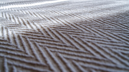 A close side view of the gray bedspread. The sun's rays illuminate the texture and weave of the fabric. A shallow depth of field.