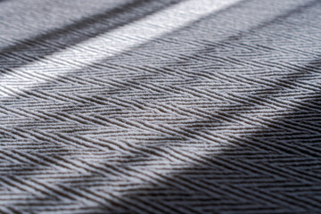 Inclined beams of light fall on a textured bedspread with a zig-zag pattern. A close-up view of the fabric. A shallow depth of field.