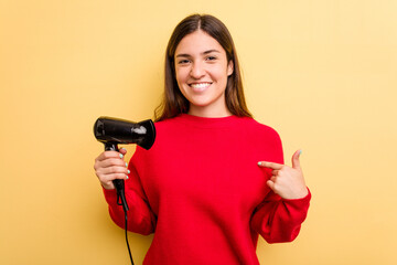 Young caucasian woman holding hairdryer isolated on yellow background person pointing by hand to a...