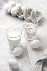 Dairy product, Glass of milk, glass of flour, eggs on grey background. Baking cake ingredients.