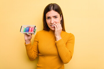 Young caucasian woman holding a batteries box isolated on yellow background biting fingernails, nervous and very anxious.