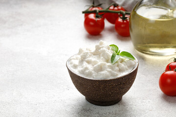 Stracciatella cheese on grey background with oil, basil and tomatoes. Curd cheese product.