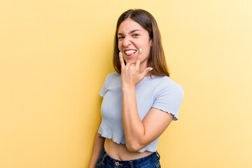 Young caucasian woman isolated on yellow background showing rock gesture with fingers