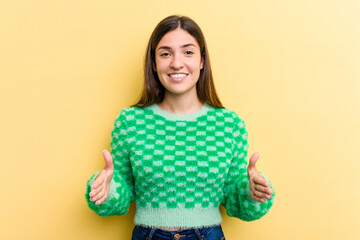 Young caucasian woman isolated on yellow background holding something with both hands, product presentation.